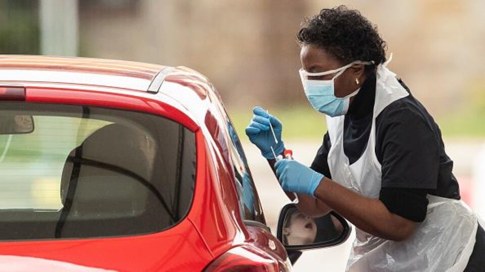 Une infirmière effectue un prélèvement sur une personne à bord d'une voiture.