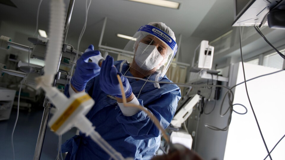 Une infirmière raccorde des tubes dans une unité de soins intensifs.