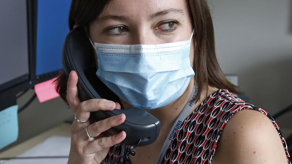 Une femme au téléphone devant un ordinateur porte un masque.
