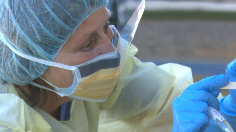 Une infirmière portant une visière et un masque effectue un test de dépistage de la COVID-19.
