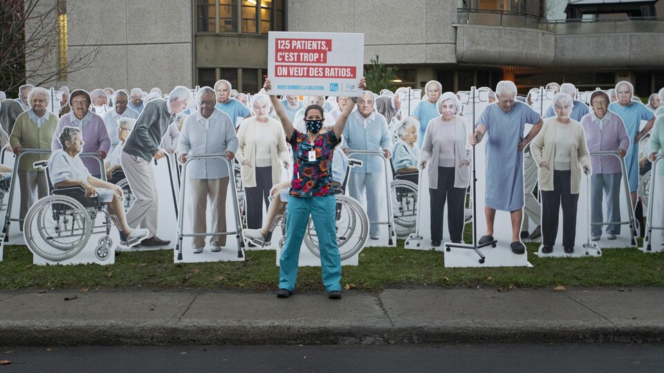 Une membre de la FIQ tient une pancarte à bout de bras et est entourée de dizaines d'effigies représentant des patients de CHSLD.