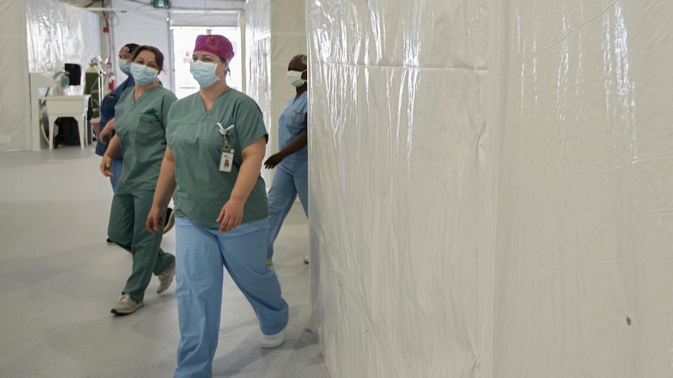 Quatre infirmières masqués marchent dans un corridor. 