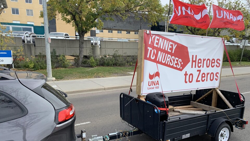 Une voiture traîne une grande pancarte en soutien aux infirmières.