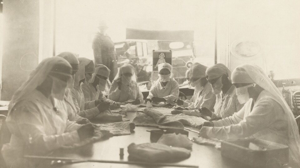 Une photo noir et blanc montre des infirmières masquées qui s'affairent à découper du tissu pour en faire des masques.
