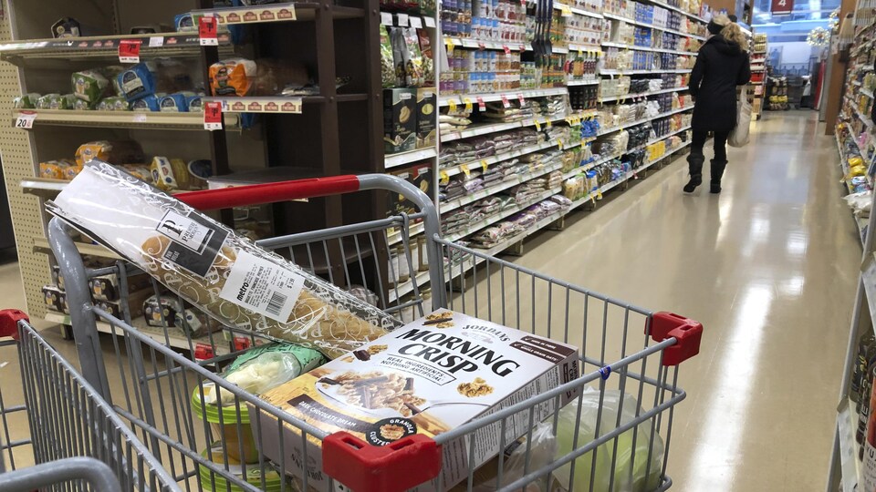 Un panier d'épicerie rempli de denrées dans une allée de supermarché.