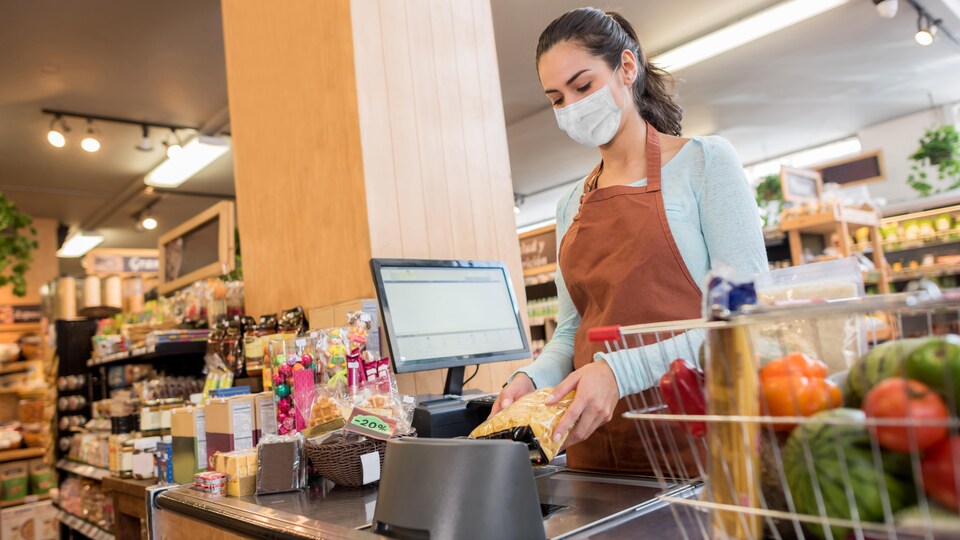 Une caissière masquée dans une épicerie.