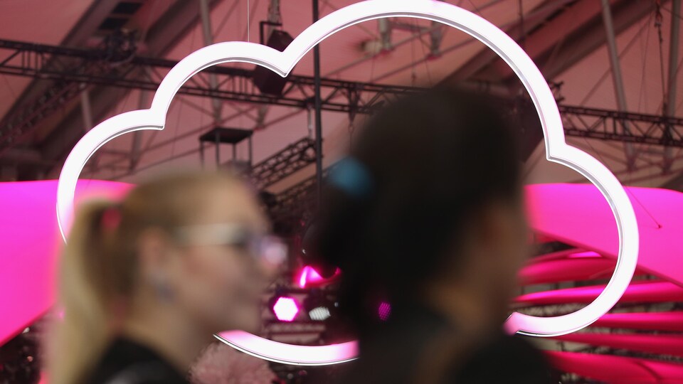 Deux femmes passent devant le logo d'un nuage suspendu au plafond d'une exposition technologique en Allemagne.