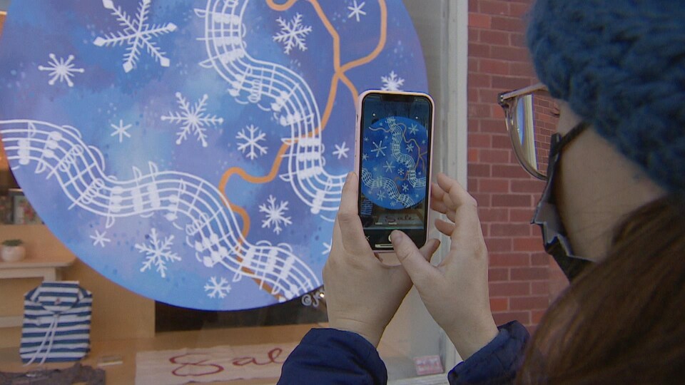 Une passante regarde une murale à travers son téléphone intelligent.