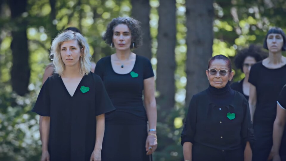 Plusieurs femmes se tiennent debout dans une forêt, portant un cœur vert sur la poitrine. 