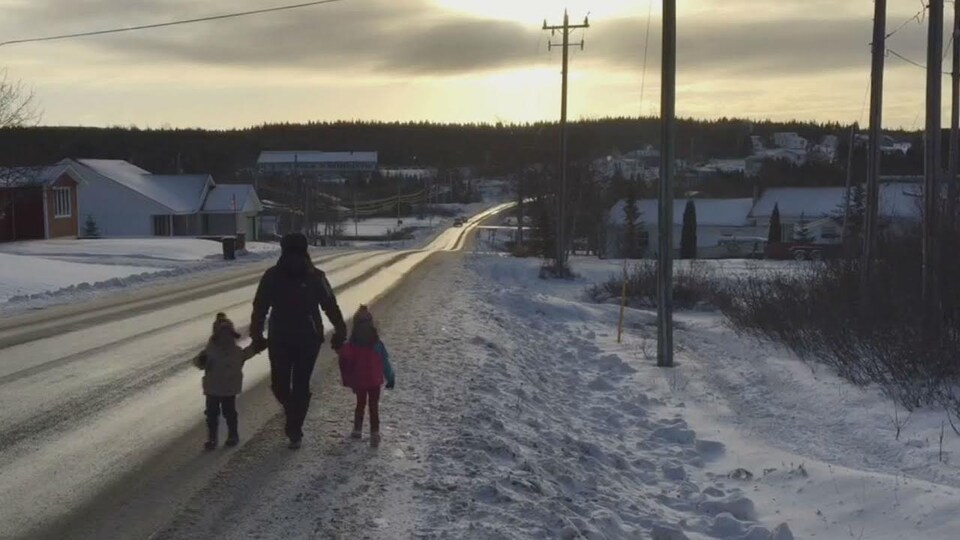 Une femme et deux enfants marchent le long d'une route dans un village en hiver.