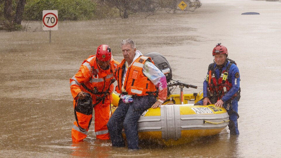 Sur une route inondée, à bord d'un bateau pneumatique, deux secouristes viennent en aide à un homme.