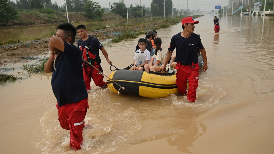 Des secours, les pieds dans l'eau, tirent un bateau pneumatique qui transporte des habitants.