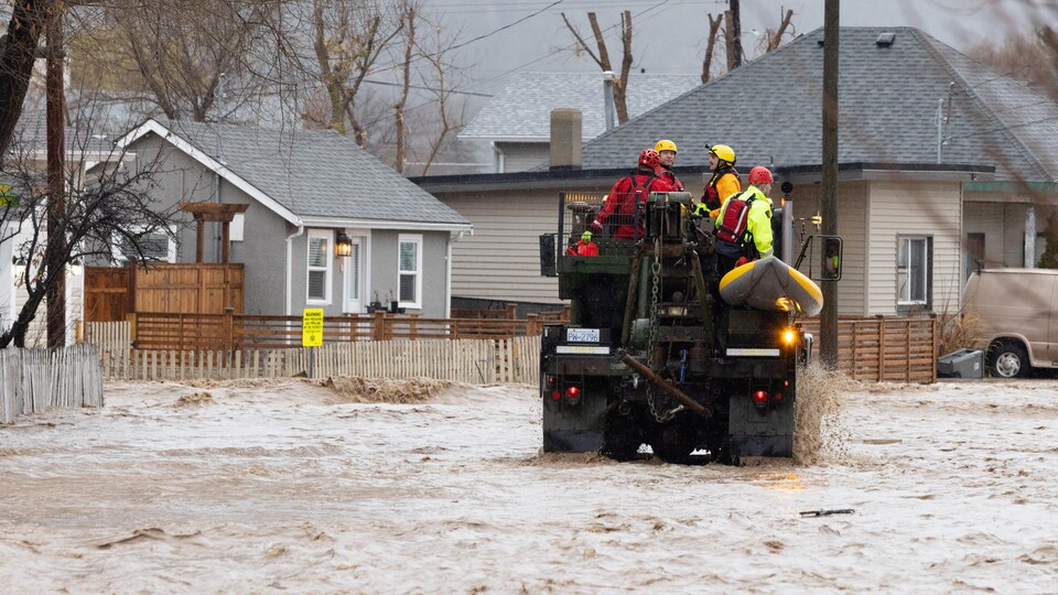Des travailleurs d'urgence sur un véhicule tout terrain dans une rue inondée, bordée de maisons.