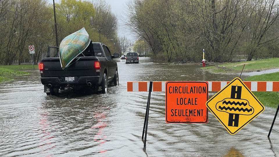 A car with a kayak on its roof rolls through the water on a marked road "Local transport only".