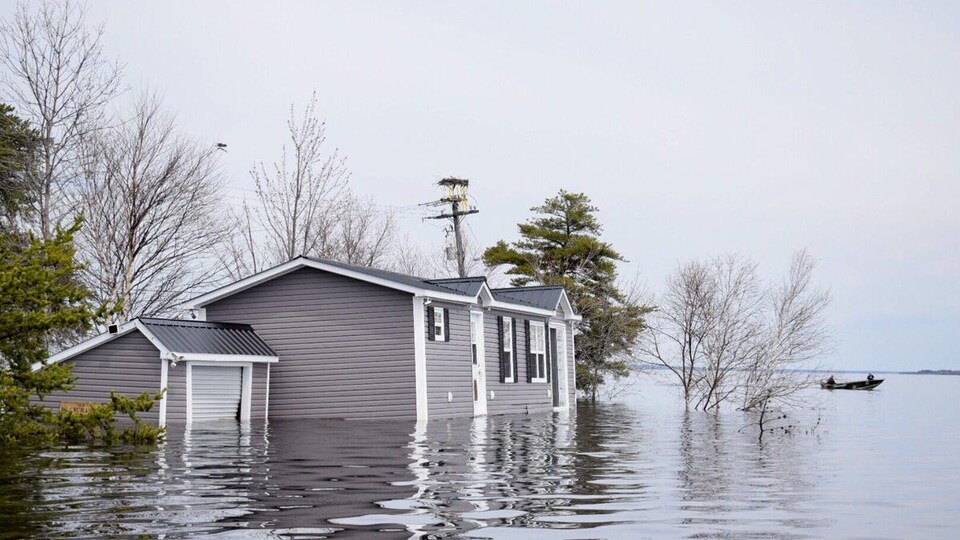 Un canot à moteur passe près d'une maison complètement inondée