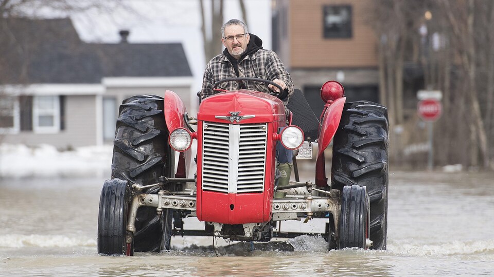 Un homme conduit un tracteur sur une rue inondée