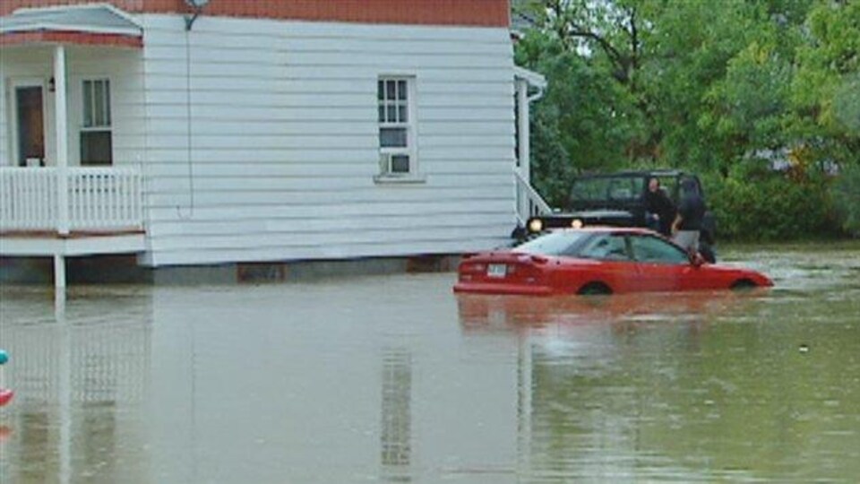 Une maison, une voiture et une Jeep lors des inondations de la rivière Lorette en 2005.