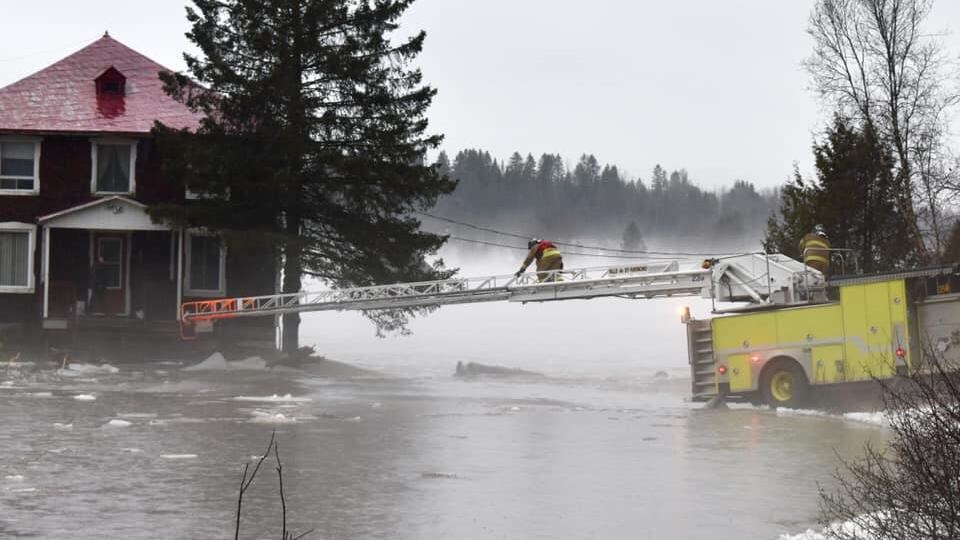 Un pompier sur une échelle s'avance vers une maison inondée