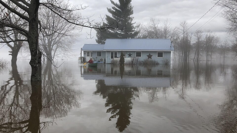 Une femme en canot devant une maison inondée à Maugerville, au Nouveau-Brunswick.