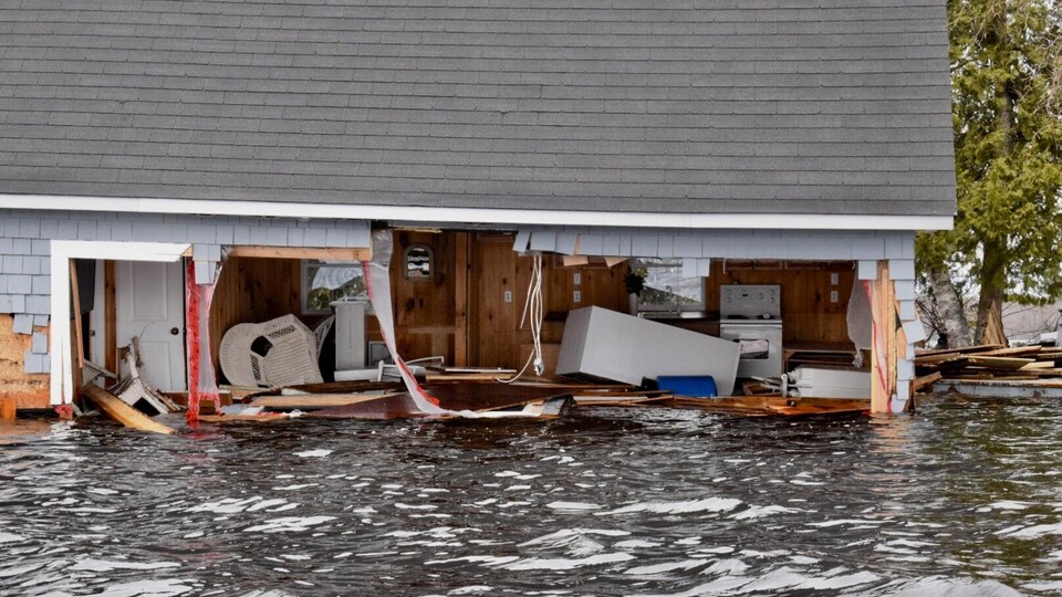 Vue de l'intérieur d'une habitation inondée dont un mur est presque complètement arraché.