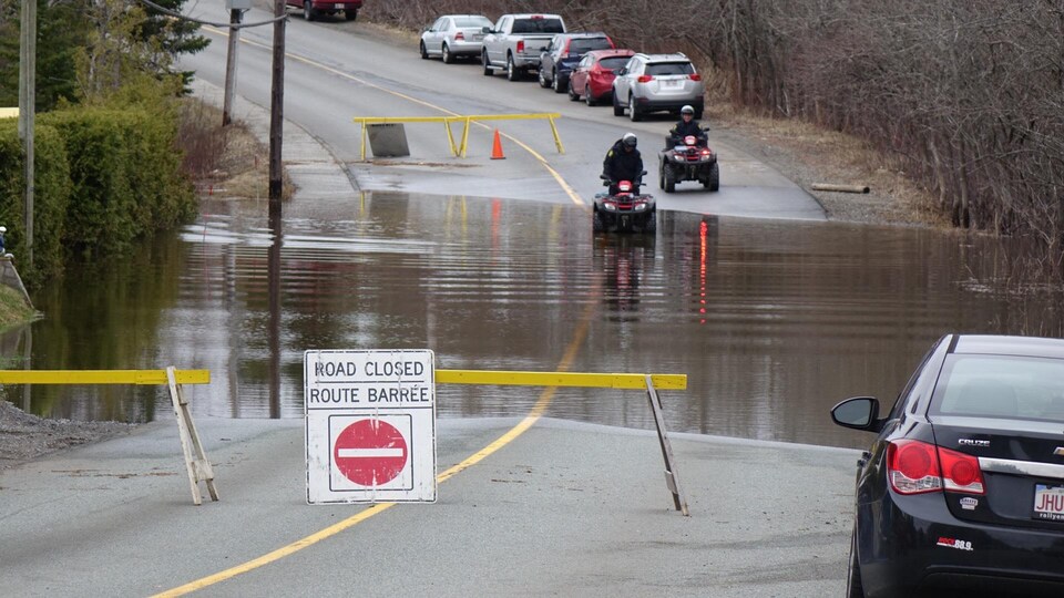 Deux personnes en VTT traversent une section de route inondée interdite à la circulation.