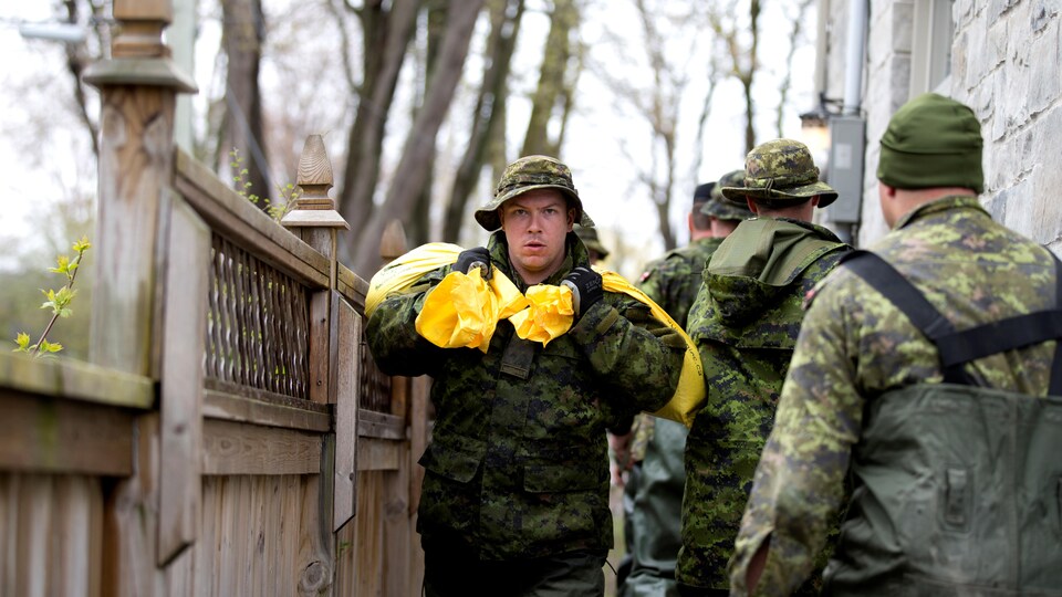 Des militaires des Forces armées canadiennes transportent des sacs de sable dans la cour d'une résidence inondée de Pierrefonds.