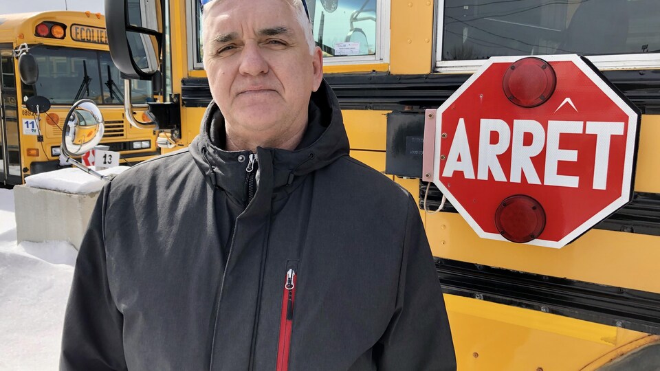 Robert Jean se tient devant un autobus scolaire. 