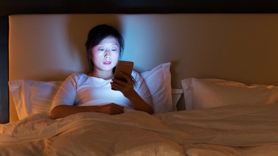 Une femme regarde son téléphone alors qu'elle est au lit la nuit.