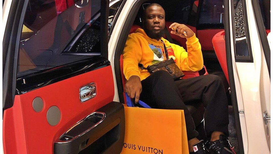 Un homme sur la banquette arrière d'une voiture de luxe avec un sac Louis Vuitton.
