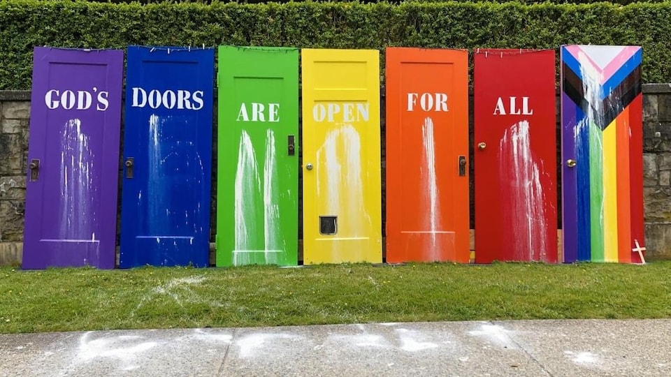Des mots écrits en anglais sur sept portes colorées forment la phrase « Les portes de Dieu sont ouvertes à tous ».
