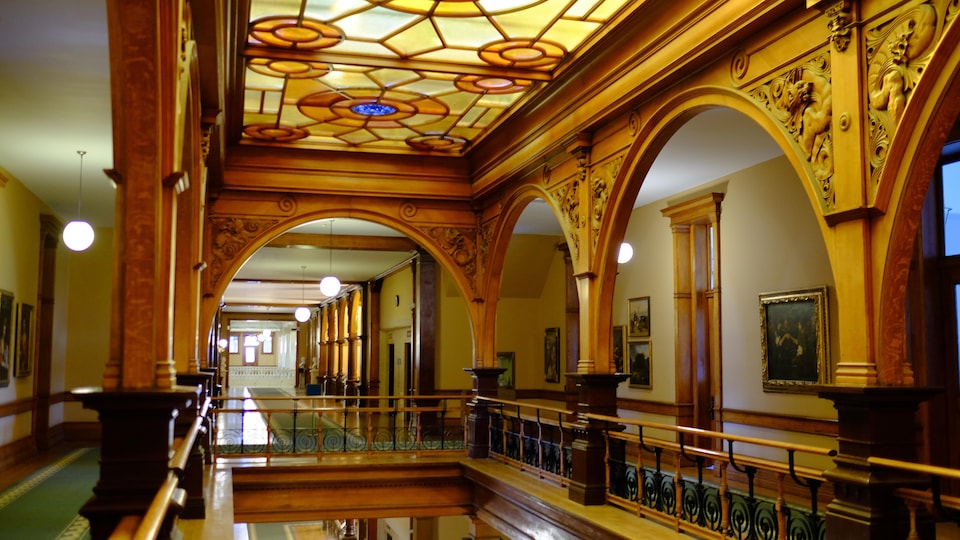 L'intérieur du parlement ontarien. De grandes colonnes de bois avec des arches et un plafond en vitrail.