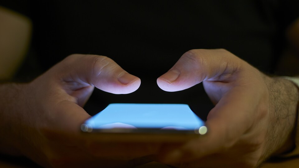 Les mains en gros plan d'un jeune homme qui utilise un téléphone cellulaire.