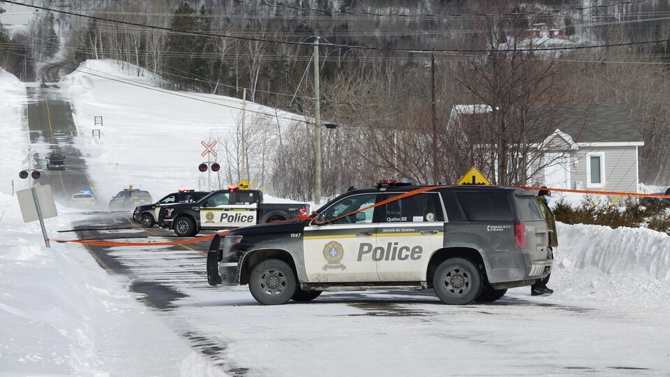 Plusieurs voitures de police sont stationnées sur un chemin enneigé.