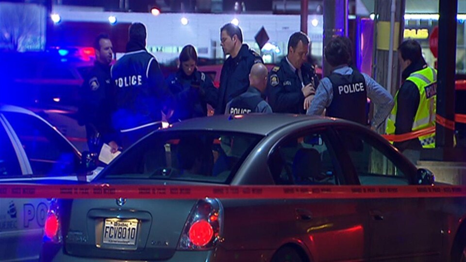 Des policiers discutent sur une scène de crime située dans le stationnement d’un commerce de restauration rapide, en soirée.