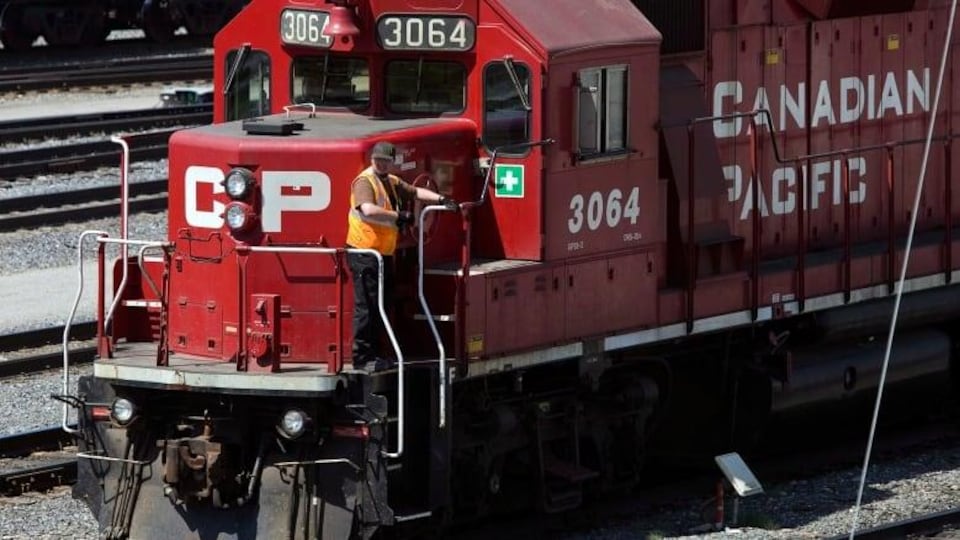 Un travailleur debout  près de la cabine du conducteur de la locomotive d'un train du Canadien Pacifique.