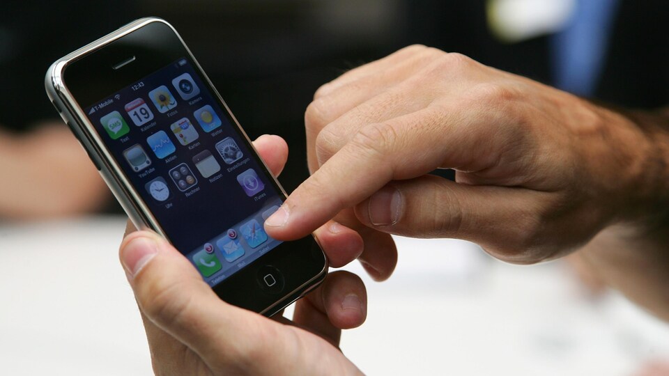 Une personne tient un iPhone dans une main et appuie sur l'écran avec l'index de son autre main.
