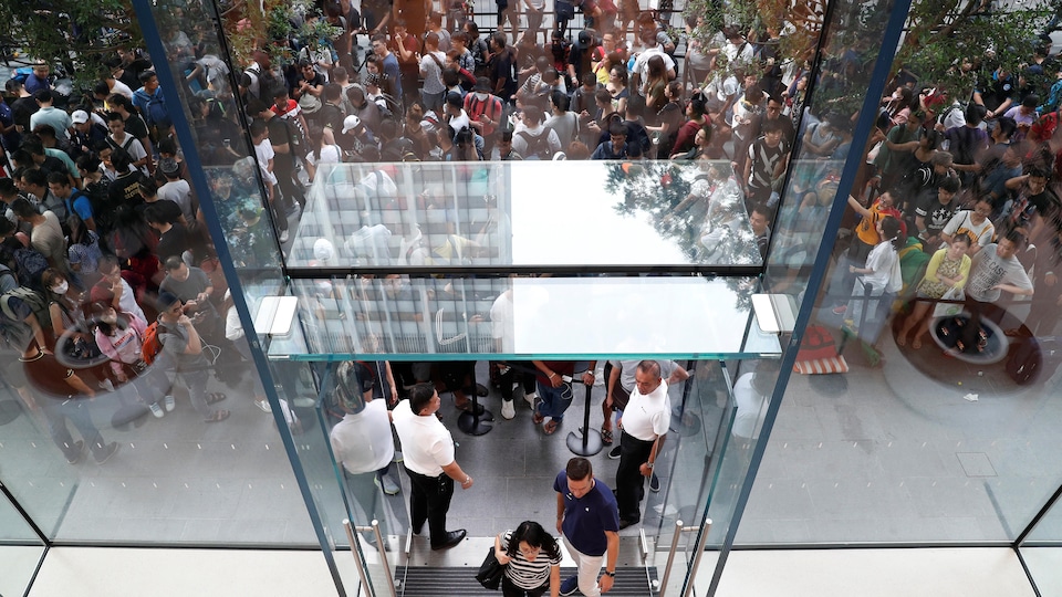 Une femme vue en plongée, entre dans un magasin Apple, alors qu'une file de personnes attendant à l'extérieur du magasin pour pouvoir rentrer.