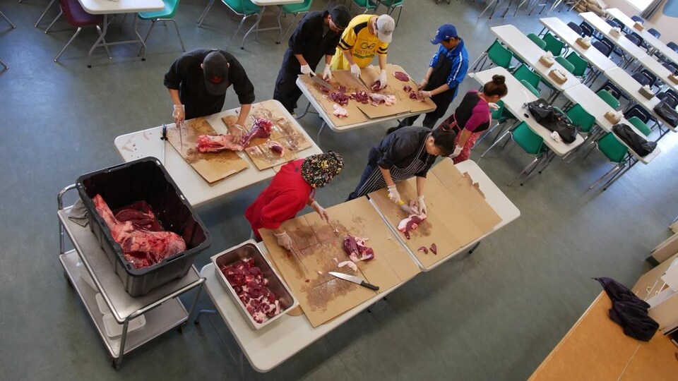 Sept personnes coupent des morceaux de viande de caribou dans le centre alimentaire d'Iqaluit.