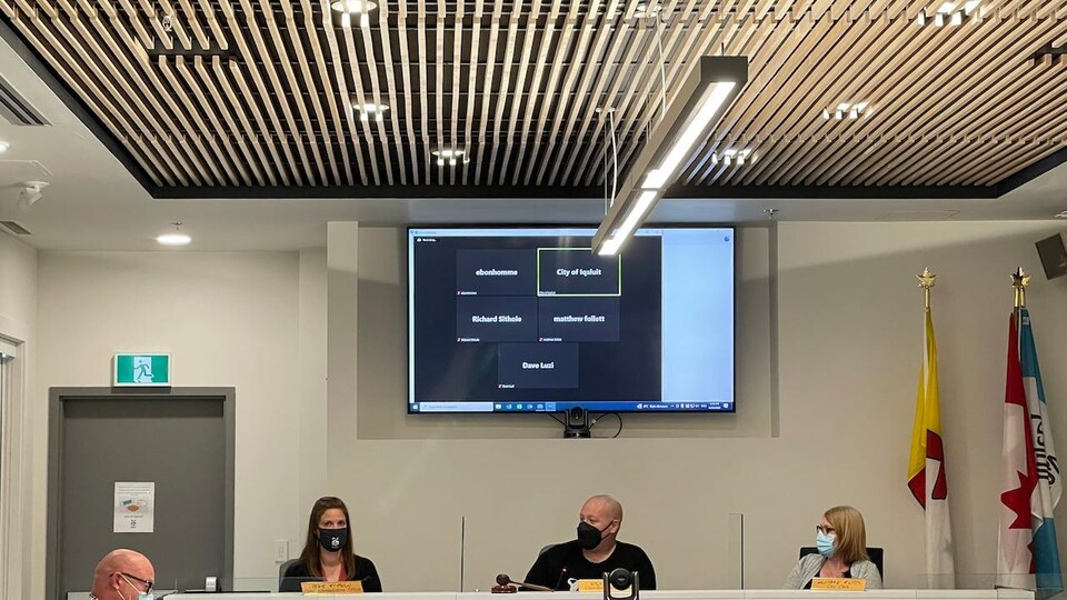 Une partie du conseil municipal d'Iqaluit assiste à une réunion en présentiel alors que les noms d'autres membres apparaissent sur un écran.