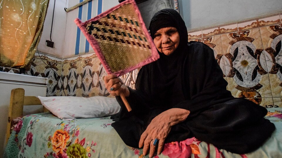 Une femme agite un éventail tandis qu'elle est assise sur un divan.