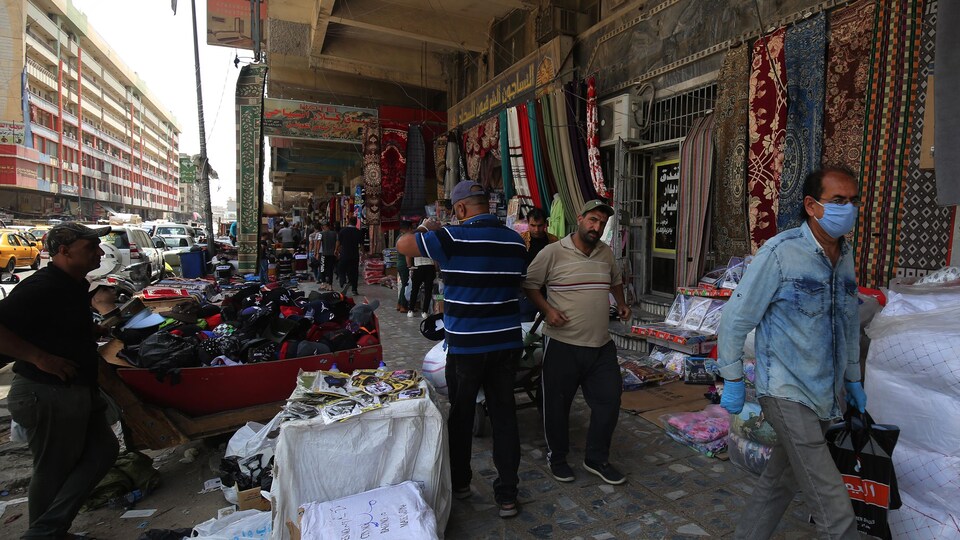 Des hommes marchent dans un marché où l'on vend des tissus et des vêtements.