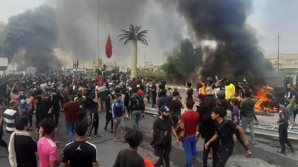 Des manifestants dans une rue et des pneus en feu avec beaucoup de fumée.