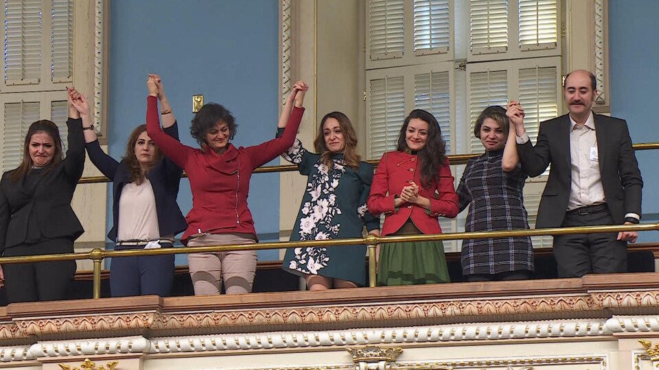 Six femmes et un homme se tenant la main dans les estrades du Salon bleu.