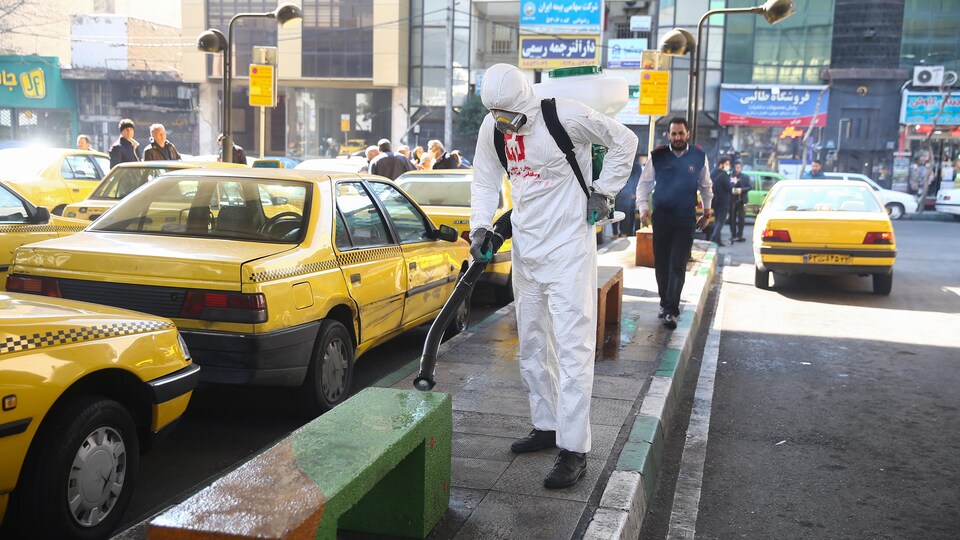 Un travailleur iranien vaporise un désinfectant sur un banc public près de nombreux taxis jaunes.