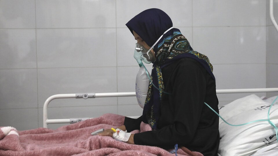Une femme avec un masque à oxygène assise dans un lit d'hôpital.