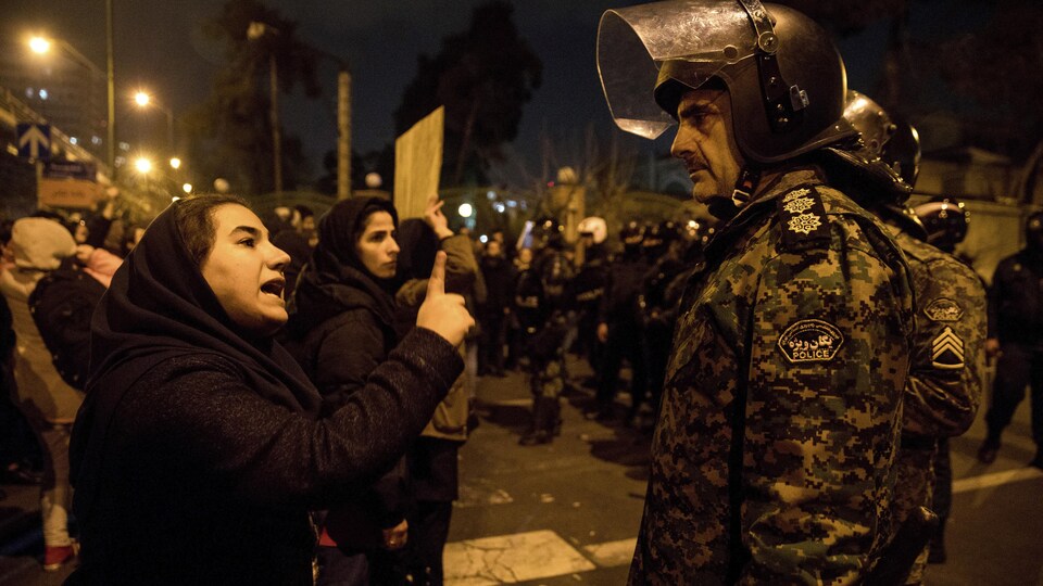 Une femme participant à une veillée aux chandelles en hommage aux victimes de l’écrasement de l’avion ukrainien parle à un policier près de l'Université Amri Kabir à Téhéran, en Iran.