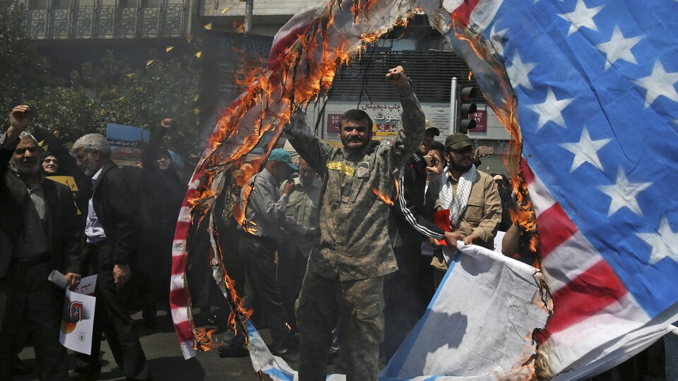 Un homme se tient les deux bras en l'air en signe de victoire alors qu'un drapeau est en feu tout près de lui.