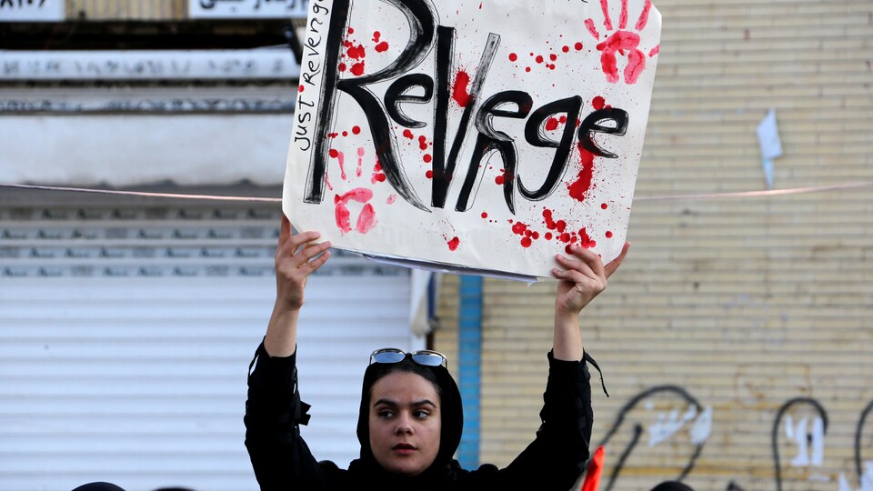 Une femme brandit par une pancarte, sur laquelle on peut voir des traces de mains ensanglantées. 