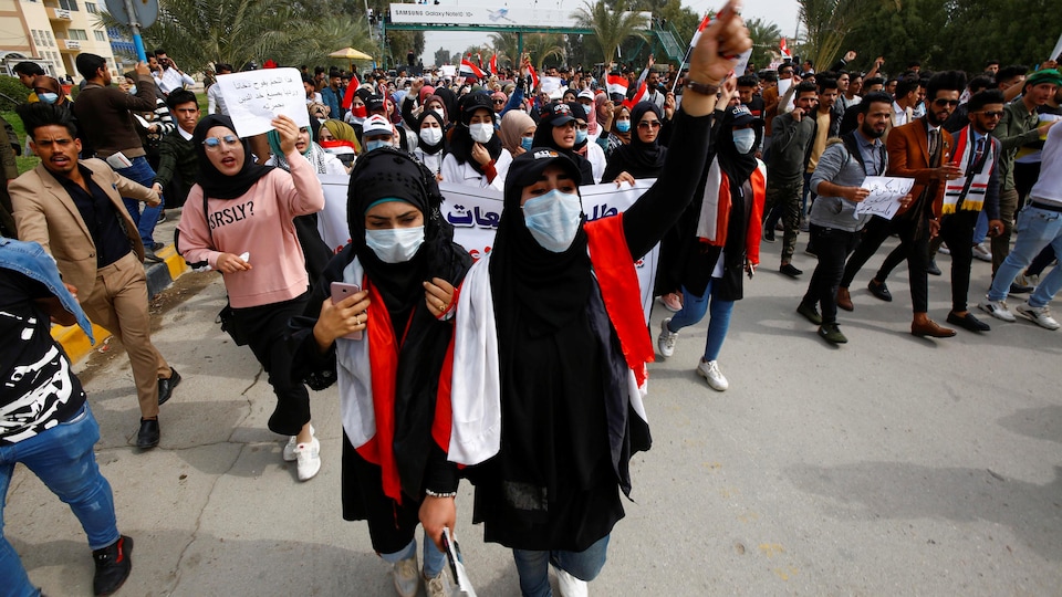Plusieurs manifestants portant des masques marchent dans une rue.