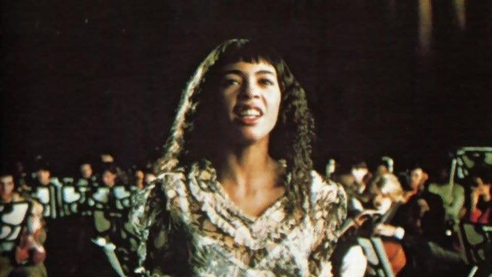 La chanteuse dans sa jeunesse est en train de chanter avec un ensemble de musiciens et de musiciennes.